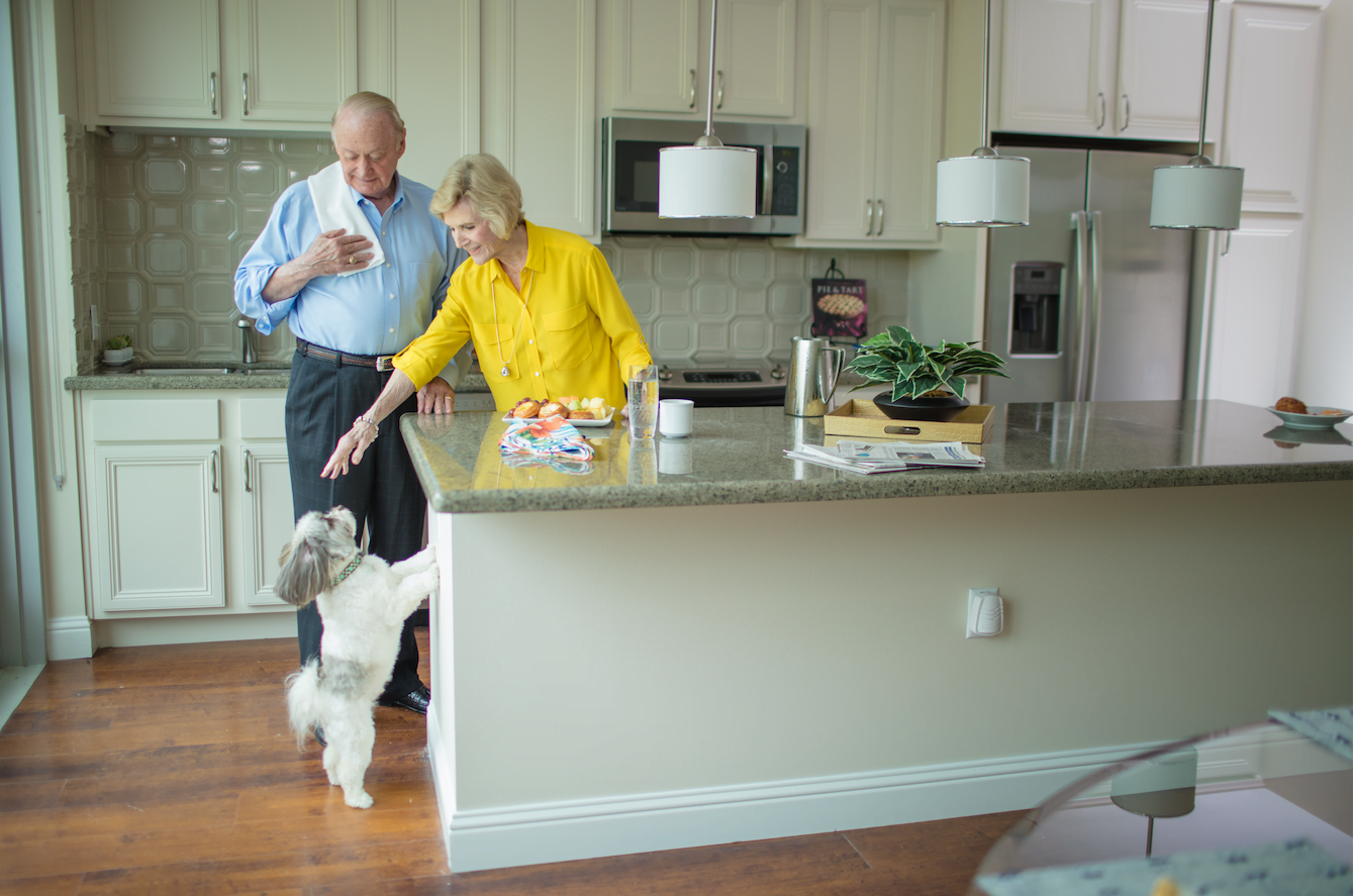 Senior couple playing with their small white dog inside their Houston senior living community