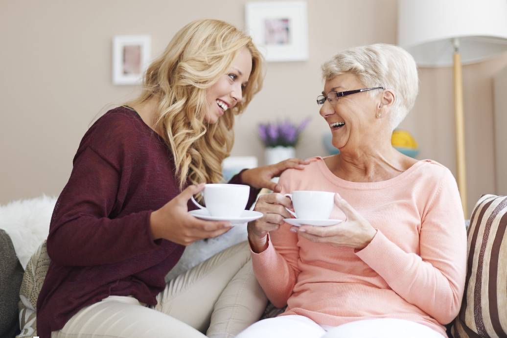 senior and adult woman talking while drinking coffee