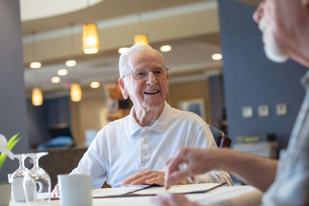 Senior gentleman seated at a table with long-term care insurance paperwork in front of him smiling