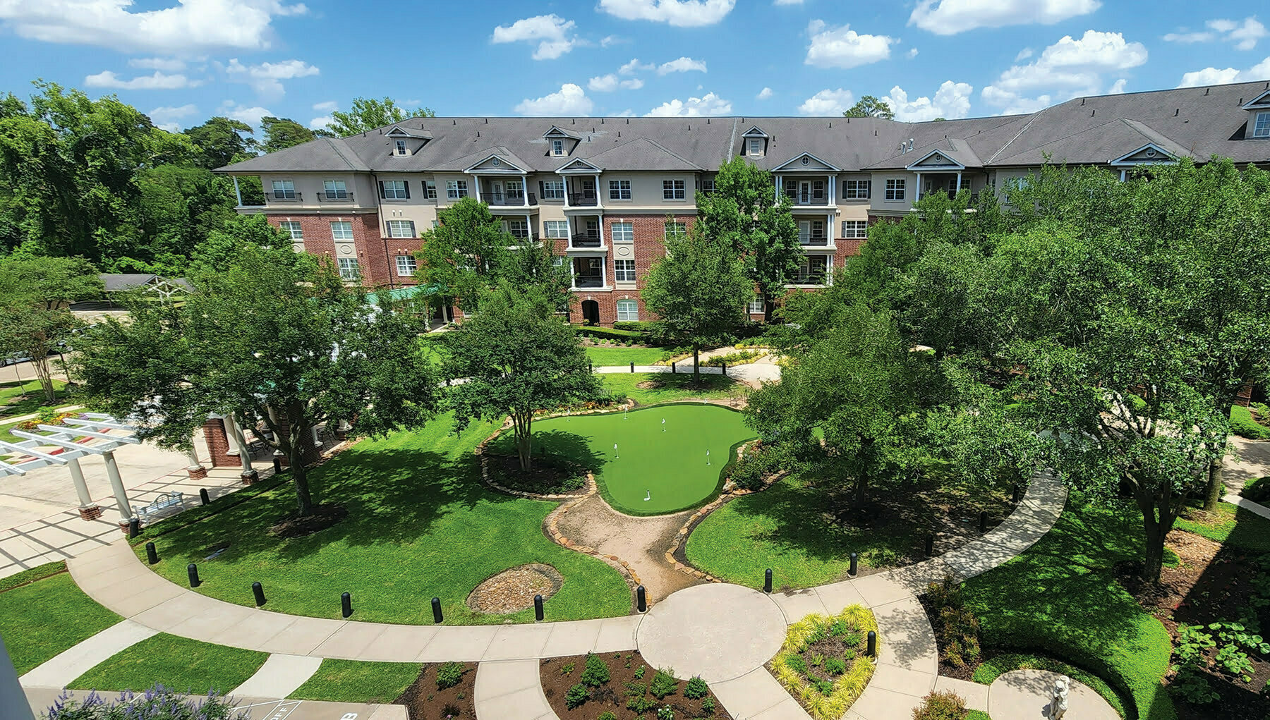 aerial view of grand courtyard sidewalks lush green grass trees in front of large senior living options