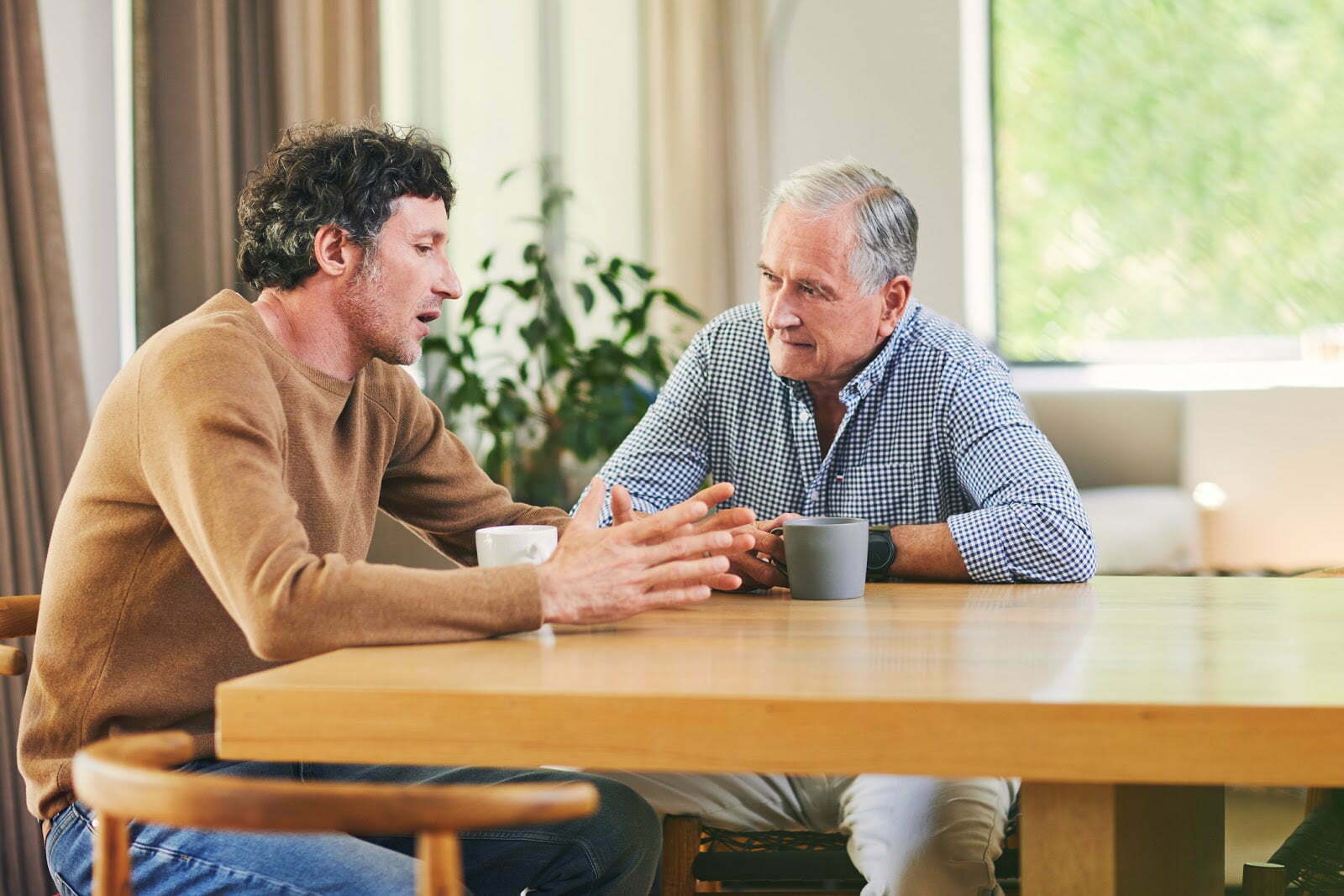 a mature man and his elderly father having coffee and a chat at home
